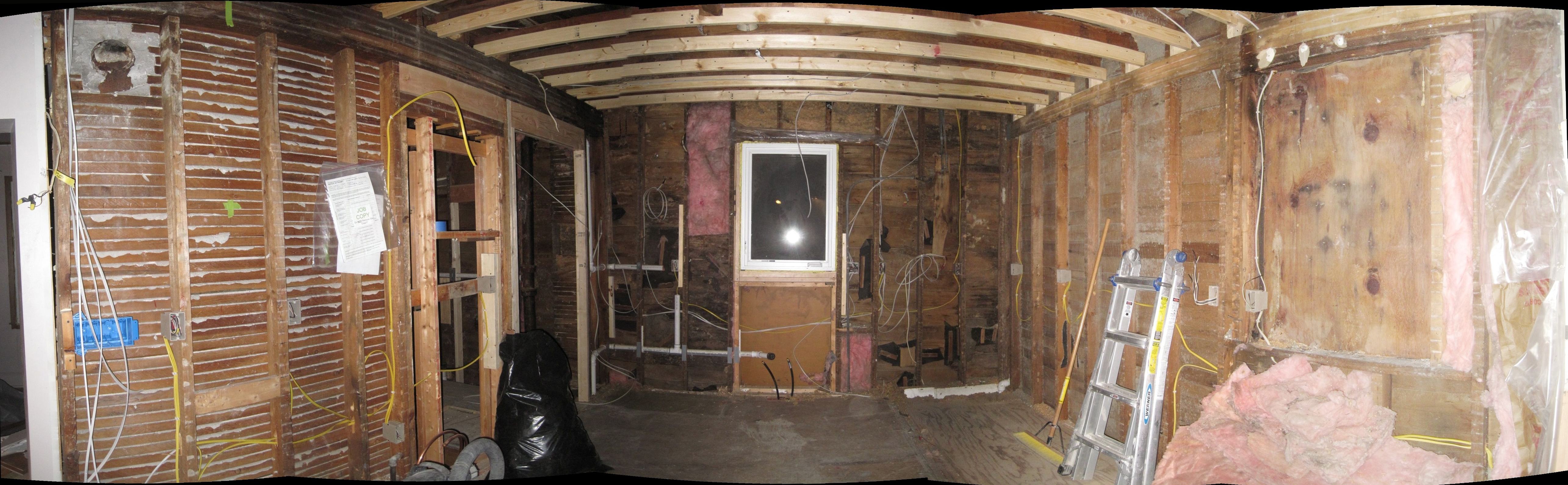 The interior of my gutted kitchen.  The wiring has started, the building permit can be seen nailed to the wall at left, next to an abandoned vent from a wood stove.